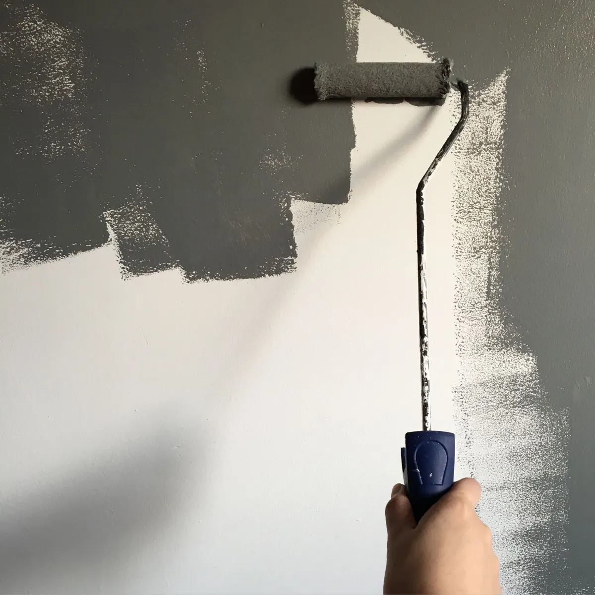 A paint roller putting a fresh coat of grey on an interior wall